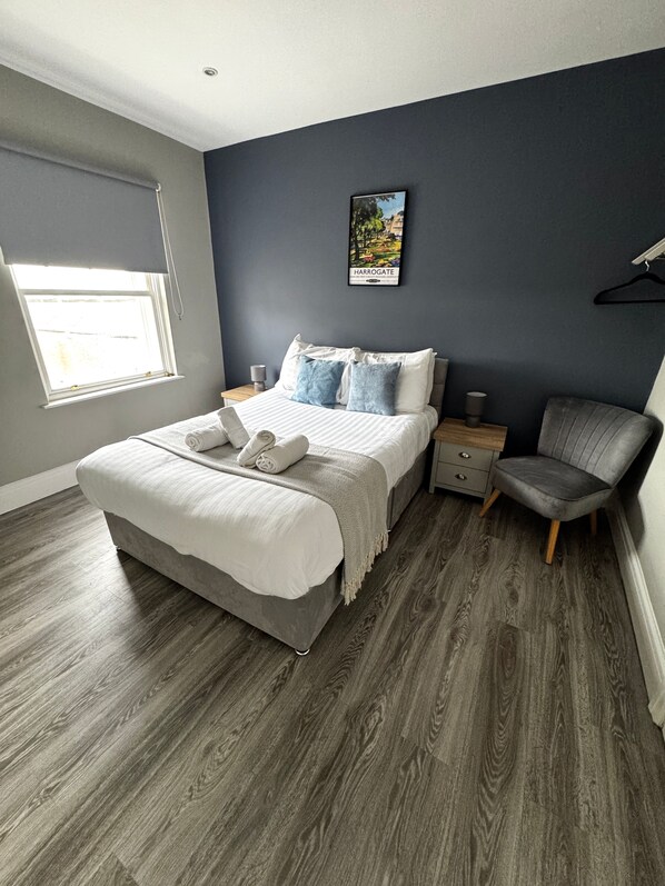 A modern bedroom with a large bed, a side table, a chair, and a window.