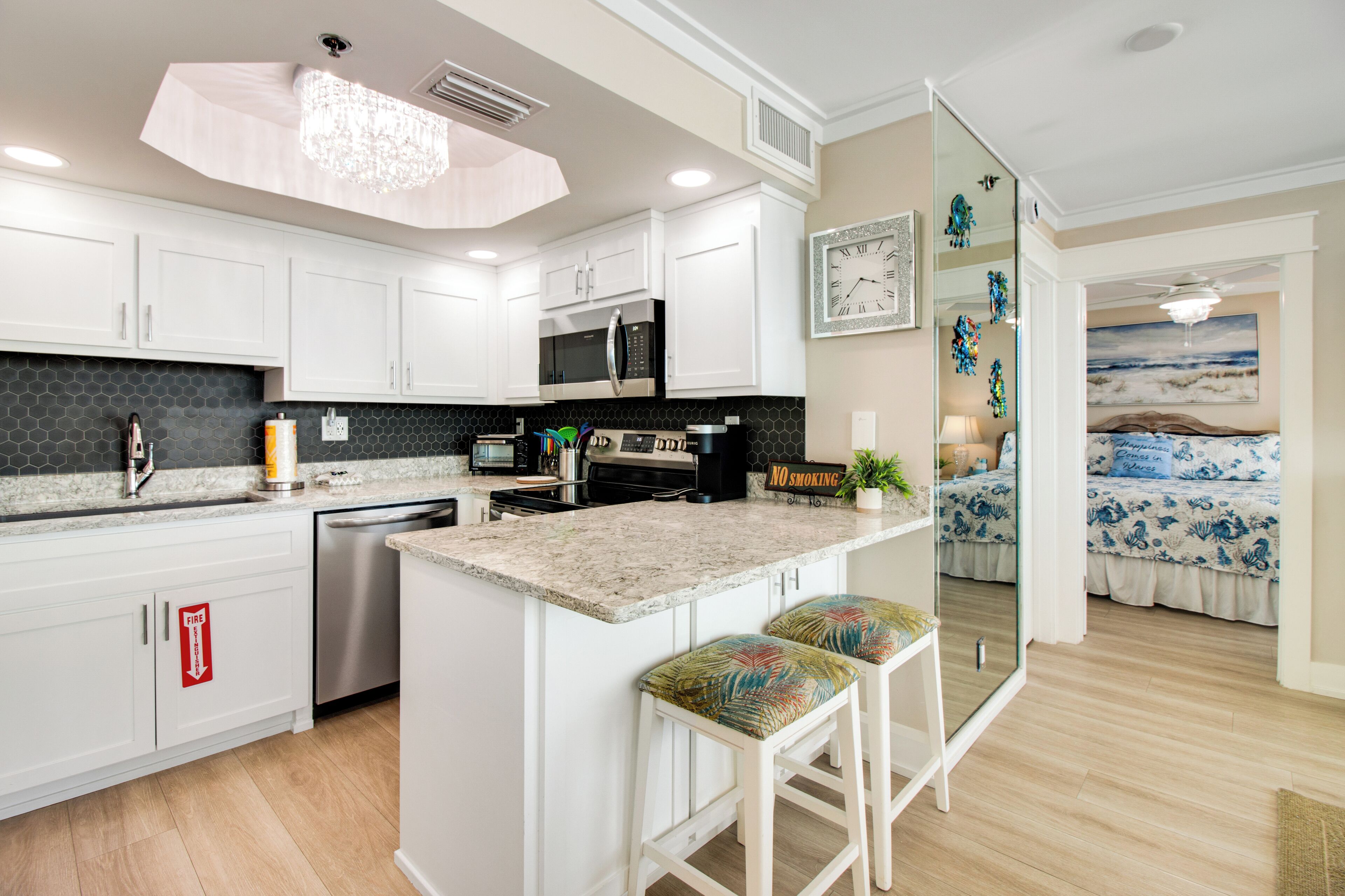 A modern kitchen with white cabinets, a granite countertop, stainless steel appliances, and a bar stool with colorful cushions.