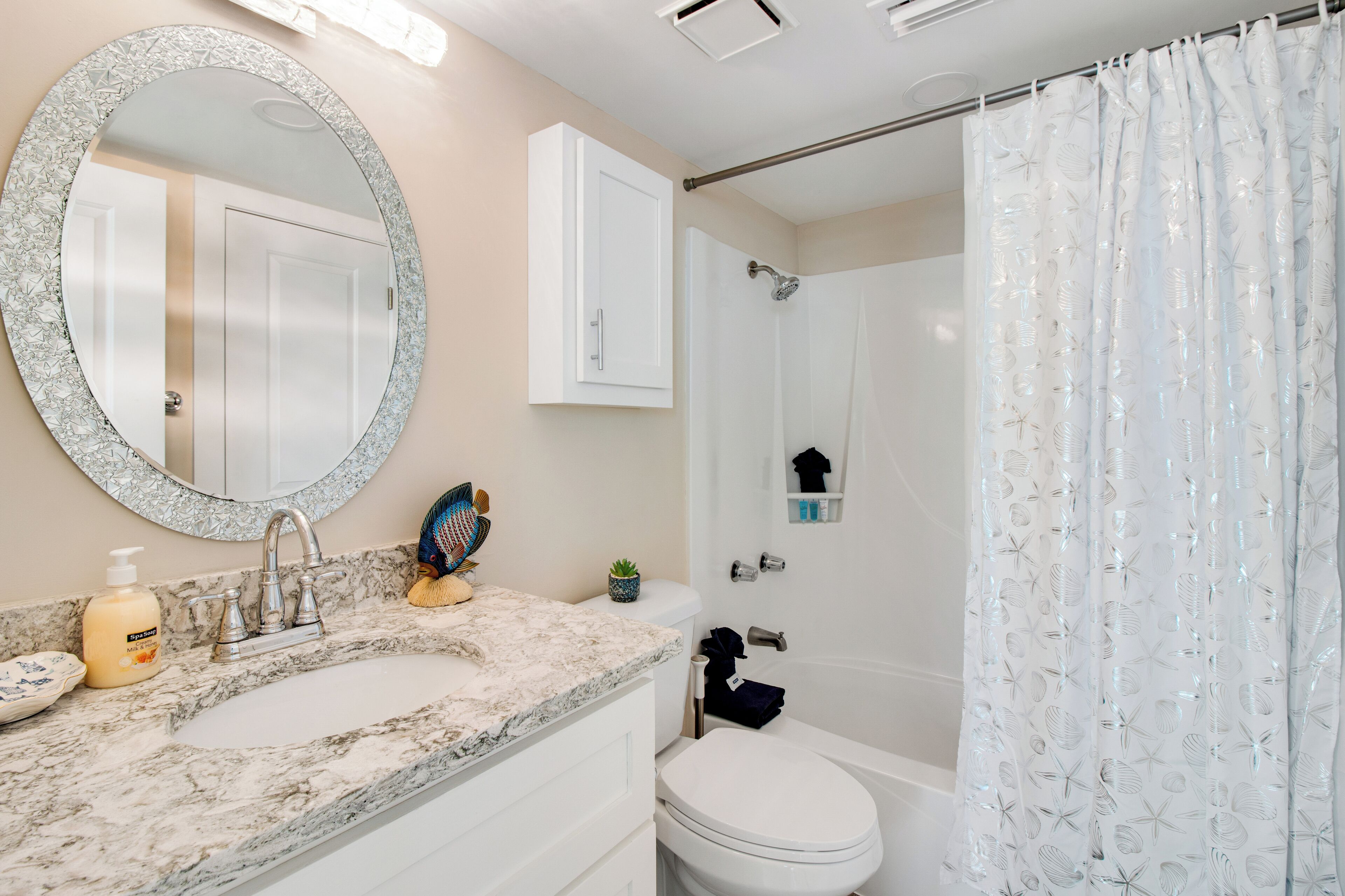 Une salle de bain avec un double lavabo, des toilettes, une douche avec un rideau, un miroir et un meuble de rangement.