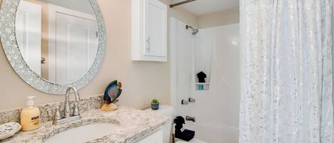 Une salle de bain avec un double lavabo, des toilettes, une douche avec un rideau, un miroir et un meuble de rangement.