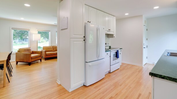A modern kitchen with white cabinetry, a refrigerator, oven, and a dining area with two sofas and a table.