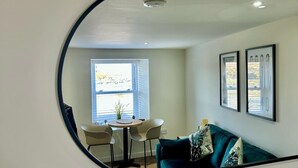 A room with a round mirror reflecting a dining area, a window, and a sofa with decorative pillows.