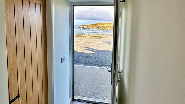 A hallway with a wooden door, a metal door, and a view of a beach through a glass door.