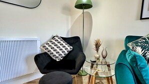 A modern living room with a black armchair, a teal sofa, a glass coffee table, and a green floor lamp.