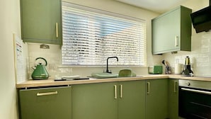 A kitchen with green cabinets, a herringbone wood floor, a window with blinds, and a built-in oven.
