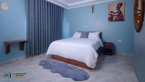 A bedroom with a bed, a nightstand, a wall-mounted shelf, a painting, and a mirror. - Juniper Park Resort (Ndaragwa)