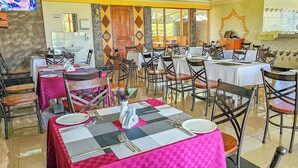A restaurant with multiple tables and chairs, a kitchen area, and a TV screen. - Juniper Park Resort (Ndaragwa)
