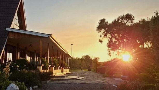A building with a covered outdoor area, a gravel path leading to it, and a sunset in the background. - Juniper Park Resort (Ndaragwa)