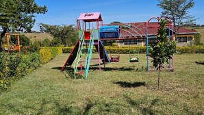 A playground with a slide, climbing structure, and swings. - Juniper Park Resort (Ndaragwa)