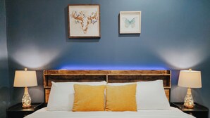 A hotel room with a bed, two nightstands, two lamps, and two framed artworks on the wall. - Convention / 3 King Beds / Jet Shower / 65" TV (Philadelphia)
