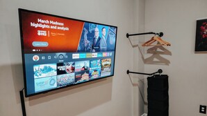 A flat-screen TV mounted on a wall displaying a sports channel interface with various sports highlights and analysis. - Convention / 3 King Beds / Jet Shower / 65" TV (Philadelphia)