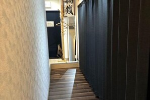 A narrow hallway with wooden flooring, a dark curtain on one side, and a wooden structure with a sign on the other. - Airandohausu (Tokyo)