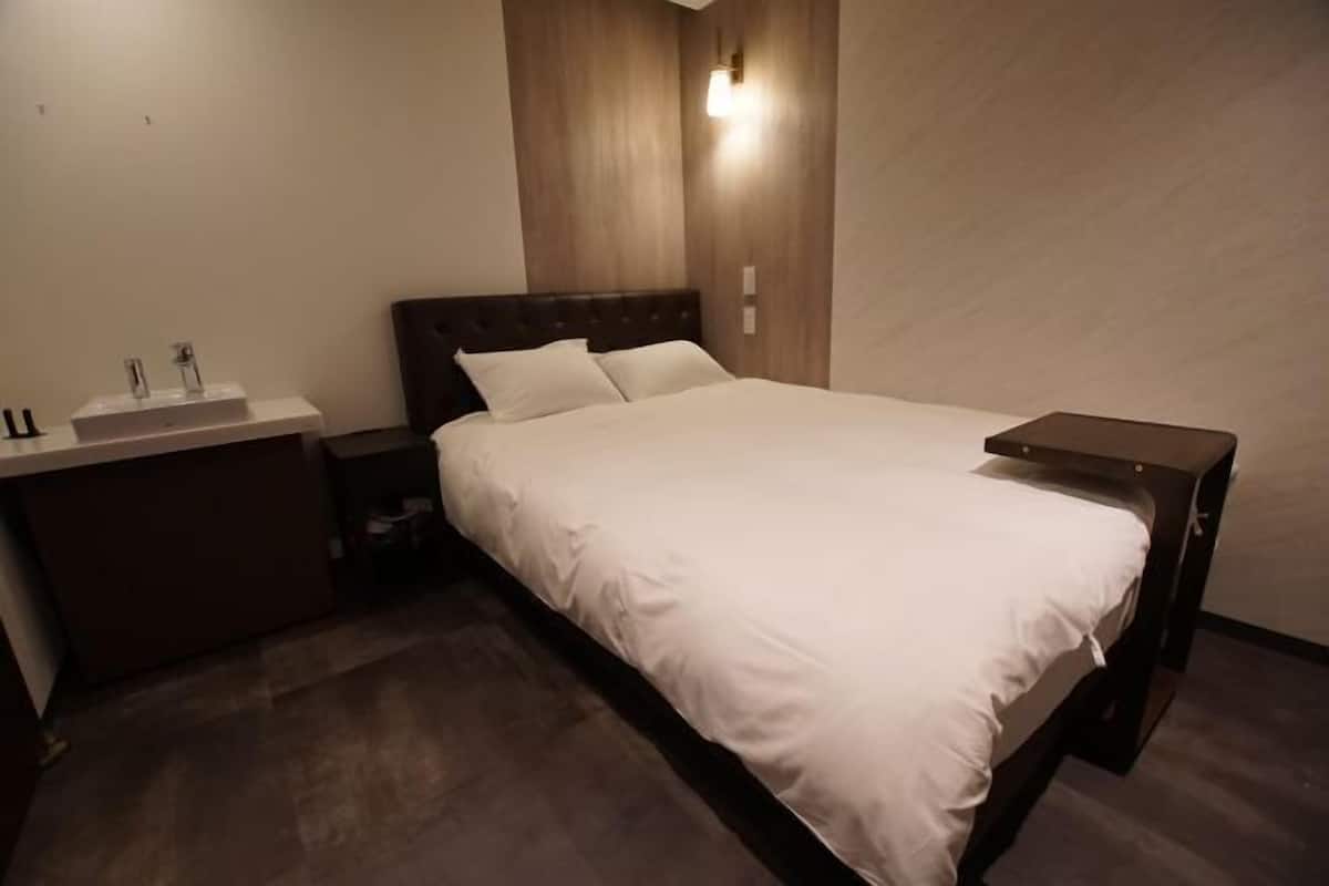 A bedroom with a bed, a bedside table, a nightstand, and a bathroom with a sink.
