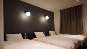 Quarto de hotel com duas camas, paredes escuras e duas luminárias fixadas na parede.