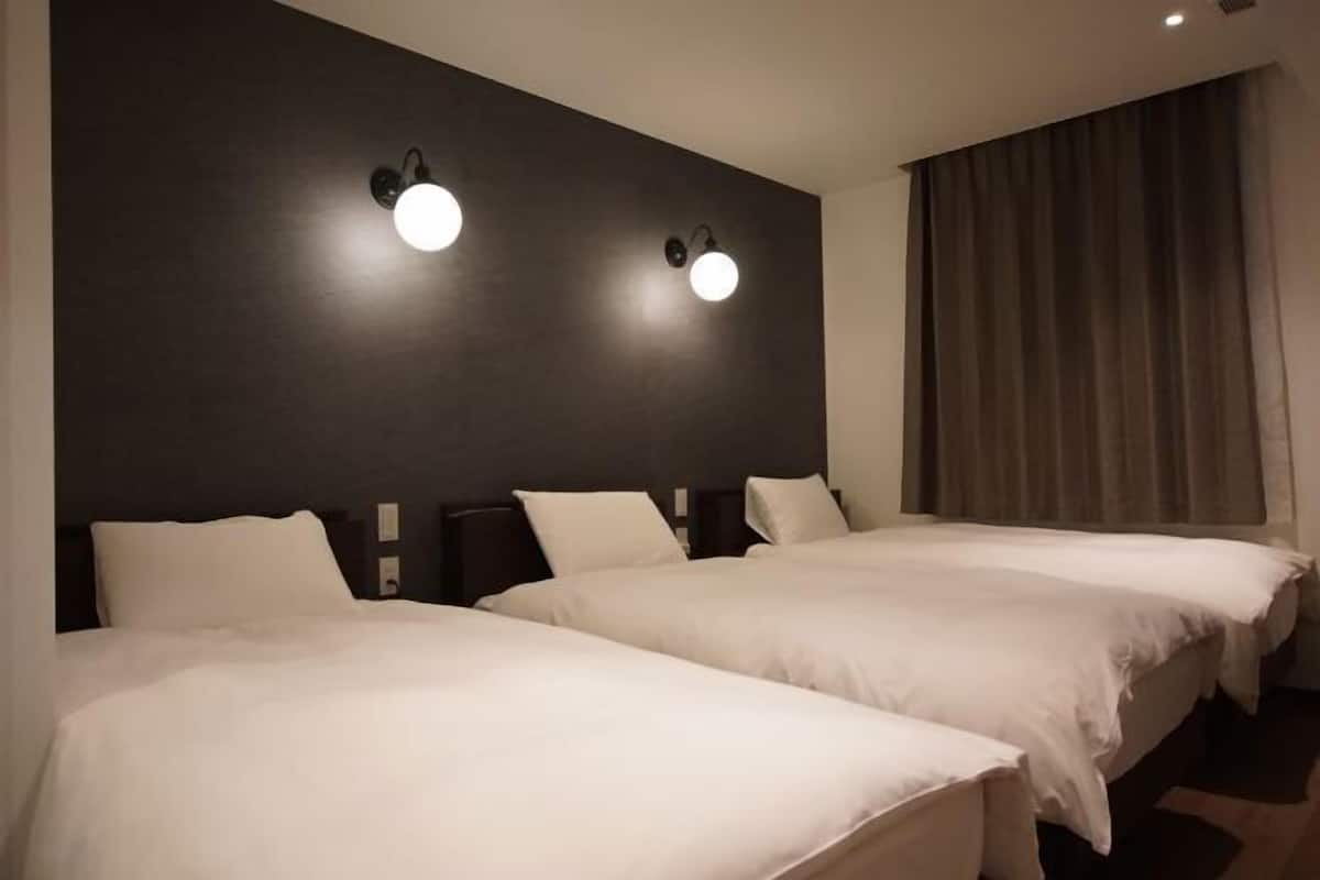 A hotel room with two beds, dark walls, and two wall-mounted lights.