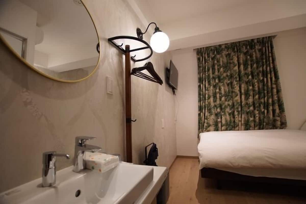 A hotel room with a white sink, a mirror, a bed, and a window with curtains.