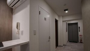 Um corredor com uma porta branca, um telefone na parede e um extintor de incêndio.