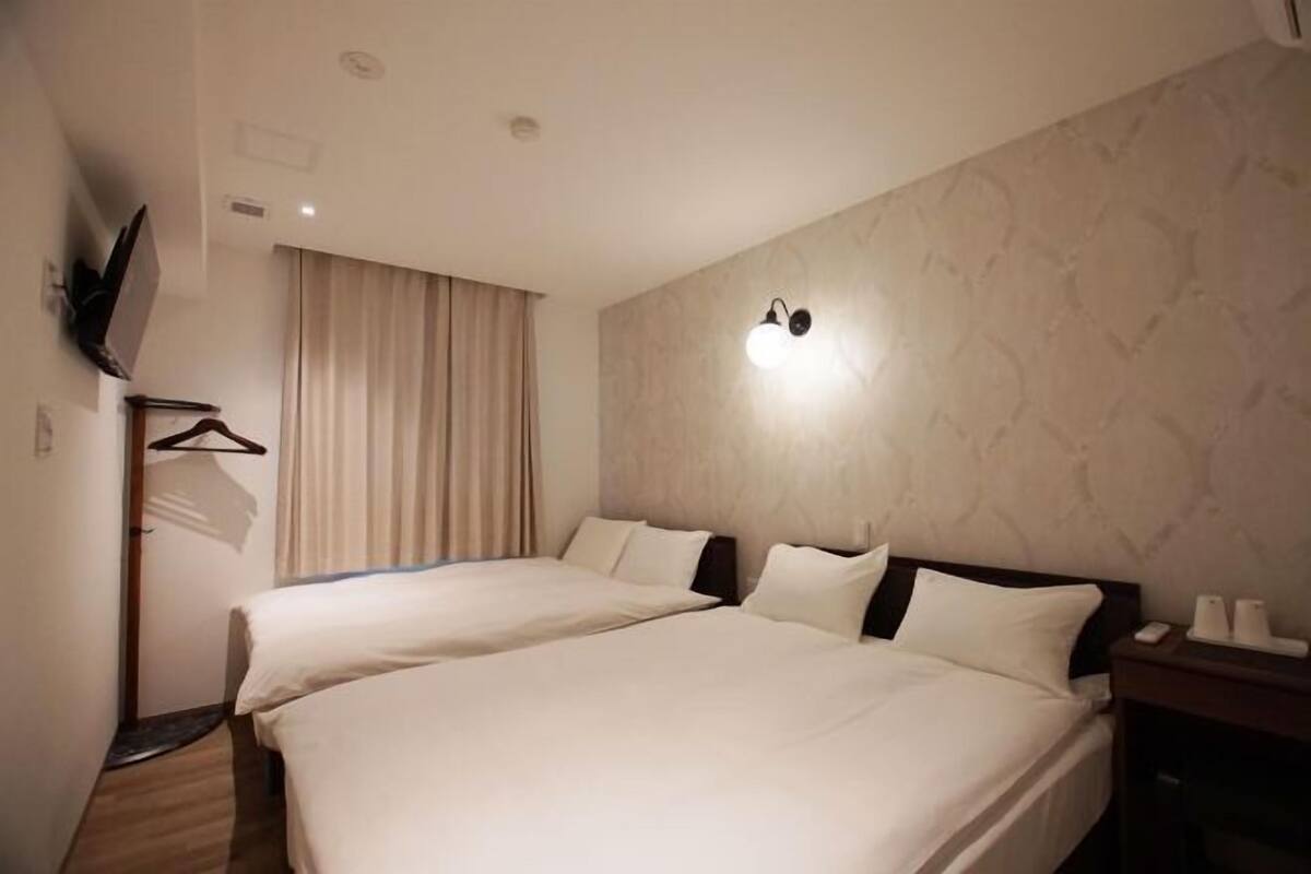 A hotel room with two beds, a TV mounted on the wall, and a bedside table with a lamp.