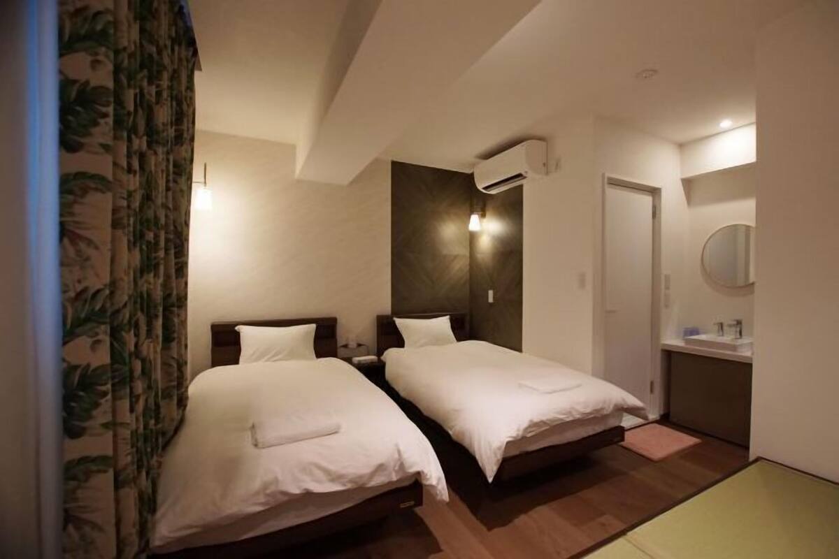 A hotel room with two beds, a small bathroom, and a ceiling-mounted air conditioner.