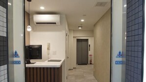 Corredor de hotel com balcão de recepção, unidade de ar condicionado e extintor de incêndio.