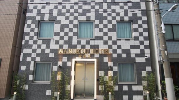 Edifício do MARUKOUHOTEL com fachada quadriculada, várias janelas e entrada central.