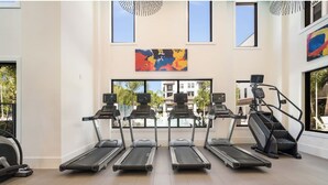 A gym with treadmills, a stair climber, and exercise equipment. There are large windows and artwork on the walls.