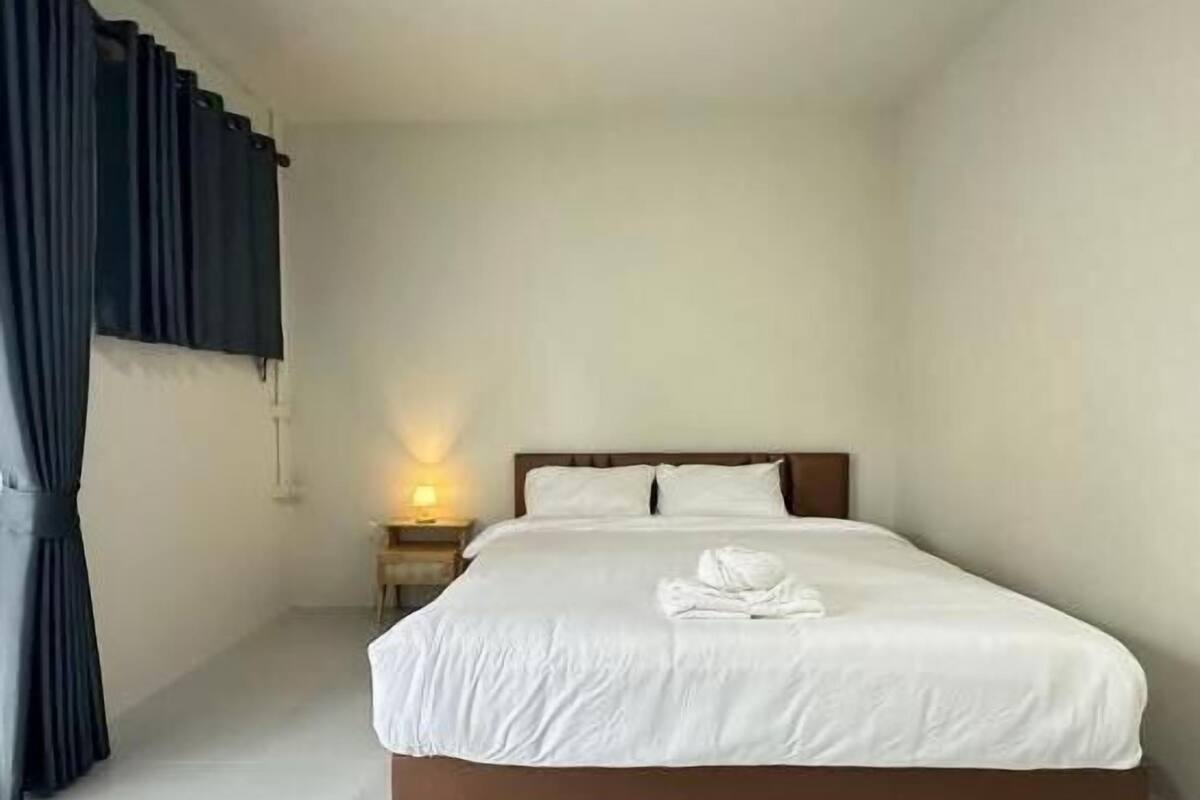 A hotel room with a single bed, a nightstand with a lamp, and a window with curtains.