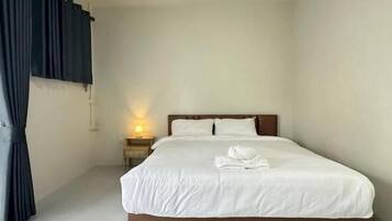 A hotel room with a single bed, a nightstand with a lamp, and a window with curtains.