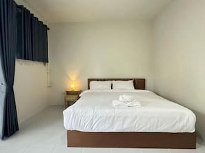 Habitación de hotel con una cama individual, una mesita de noche con lámpara y una ventana con cortinas.