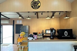 L’intérieur d’un café, avec un mur en bois, un comptoir où se trouve une machine à café, et une enseigne au-dessus du comptoir.
