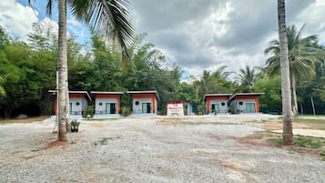 A row of single-story buildings with a gravel driveway, surrounded by palm trees and greenery.
