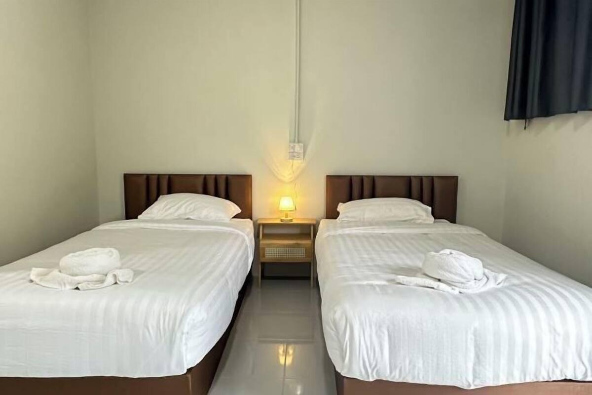 A hotel room with two single beds, a nightstand with a lamp, and a wall-mounted light fixture.