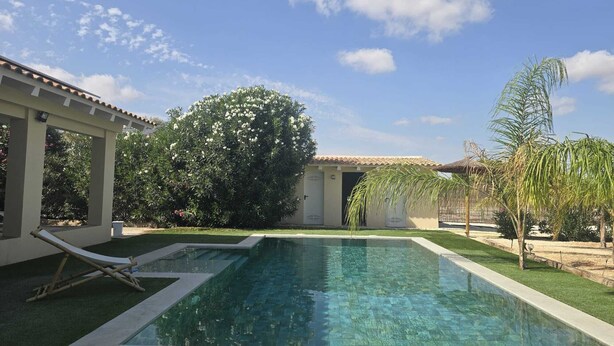 Ein Pool mit Fliesenveranda, Liegestuhl und einer Pergola.