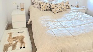 Ein Schlafzimmer mit Bett, Nachttisch, Lampe, Fenster mit Jalousien und Teppich mit Löwenmuster.