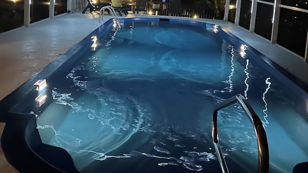 Un jacuzzi con cerramiento de vidrio, rodeado de sillas y mesas, bajo una zona cubierta con vistas al cielo nocturno.