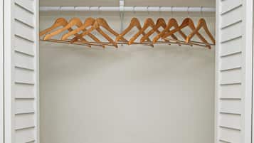 A closet with white shutters, wooden hangers, a stack of white towels, and a wicker basket.