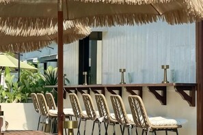 A covered outdoor seating area with chairs and tables, a thatched umbrella, and a view of a building in the background. - The Palm Suite Tanjung Tokong (Tanjung Tokong)