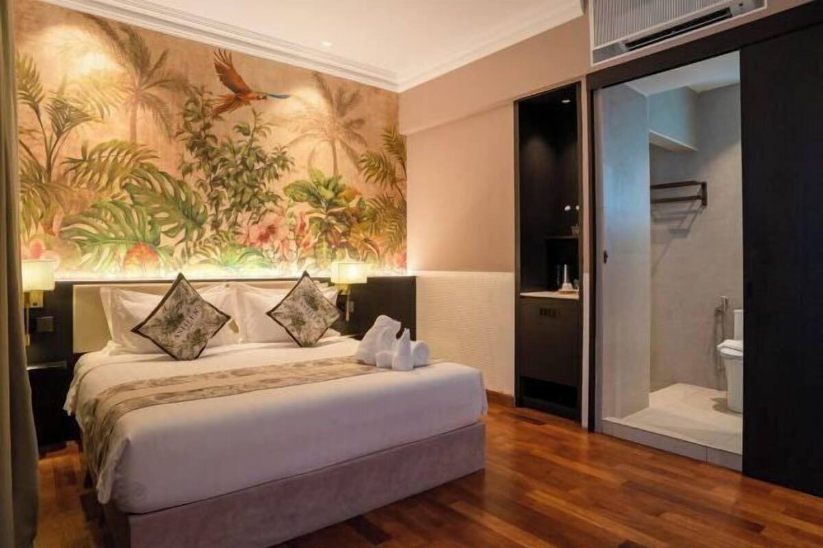 Ein Hotelzimmer mit Bett, einem tropischen Wandbild, einem begehbaren Kleiderschrank und einer Duschkabine.