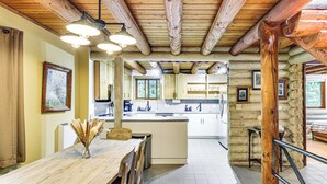 Eine rustikale Küche mit Holzbalken, einem Essbereich mit Holztisch und Blick auf den Wohnbereich.