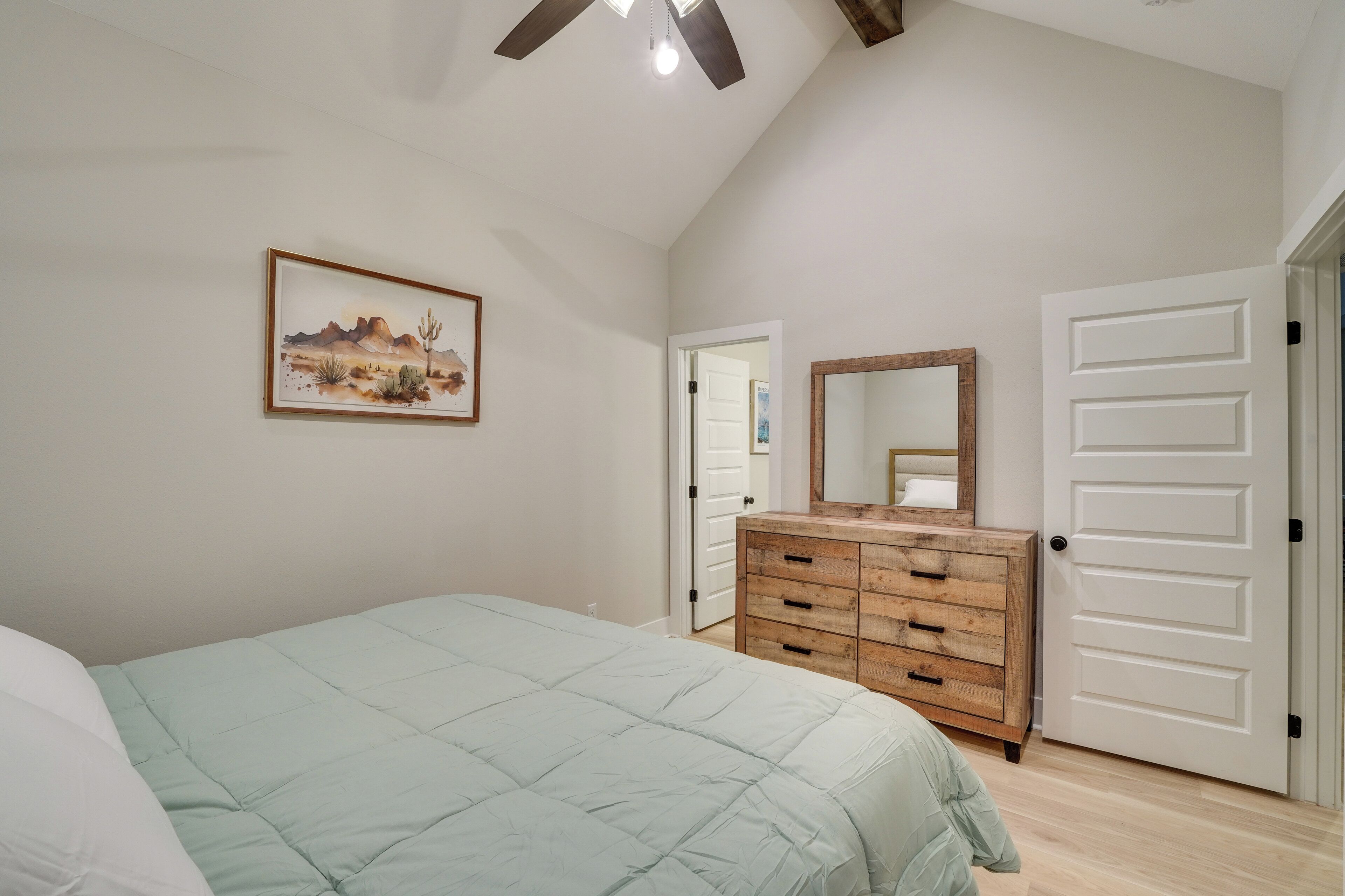 Une chambre à coucher avec un lit, une commode, un miroir et une porte.