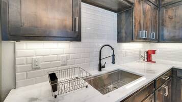 A modern kitchen with dark wooden cabinets, white subway tiles, a stainless steel sink, and a red coffee maker.