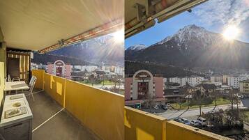 Un balcon avec une balustrade jaune donnant sur une ville et des montagnes.