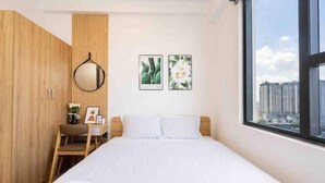 A bedroom with a bed, a wooden wardrobe, a desk with a chair, and two framed pictures on the wall.