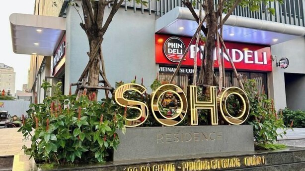A sign for 'SOHO RESIDENCE' with a large gold 'SOHO' lettering, a 'PHIN DELI' sign in the background, and a building facade.