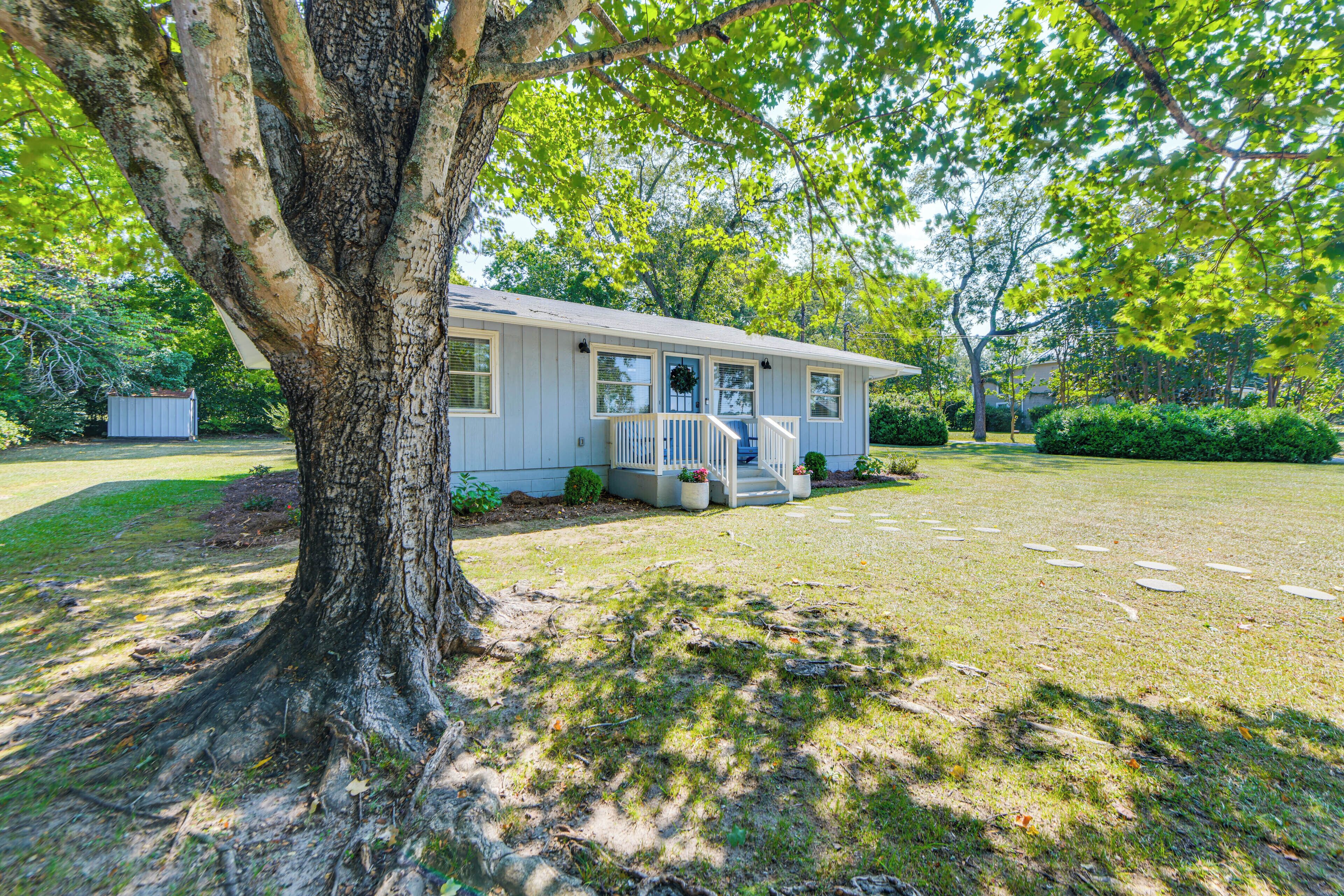 A single-story house with a front porch, a small garden, and a large tree in the foreground.