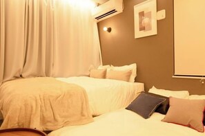 Habitación de hotel con dos camas, un ventanal con cortinas, un equipo de aire acondicionado y un cuadro colgado en la pared.