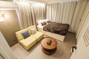 Una habitación de hotel con cama, sofá, una mesita redonda y cortinas.