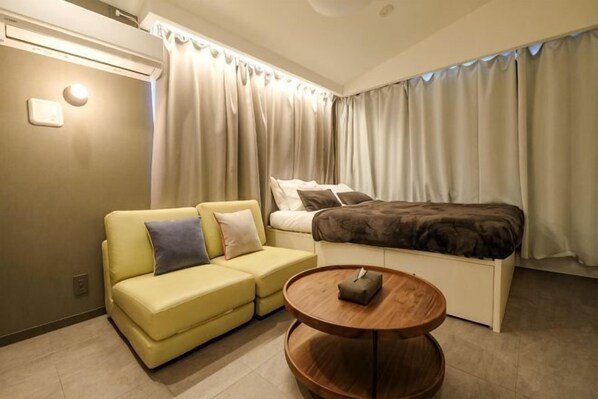 Una habitación de hotel con cama, sofá, una mesita y cortinas.
