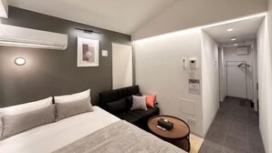 A modern hotel room with a bed, a small sofa, a round table, and a shower area. - Fandina E Resort (Kamakura)