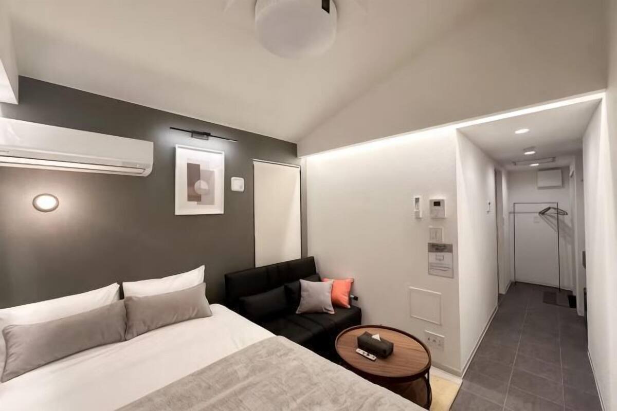 Ein modernes Hotelzimmer mit Bett, einer kleinen Couch, einem runden Tisch und einer Duschkabine.